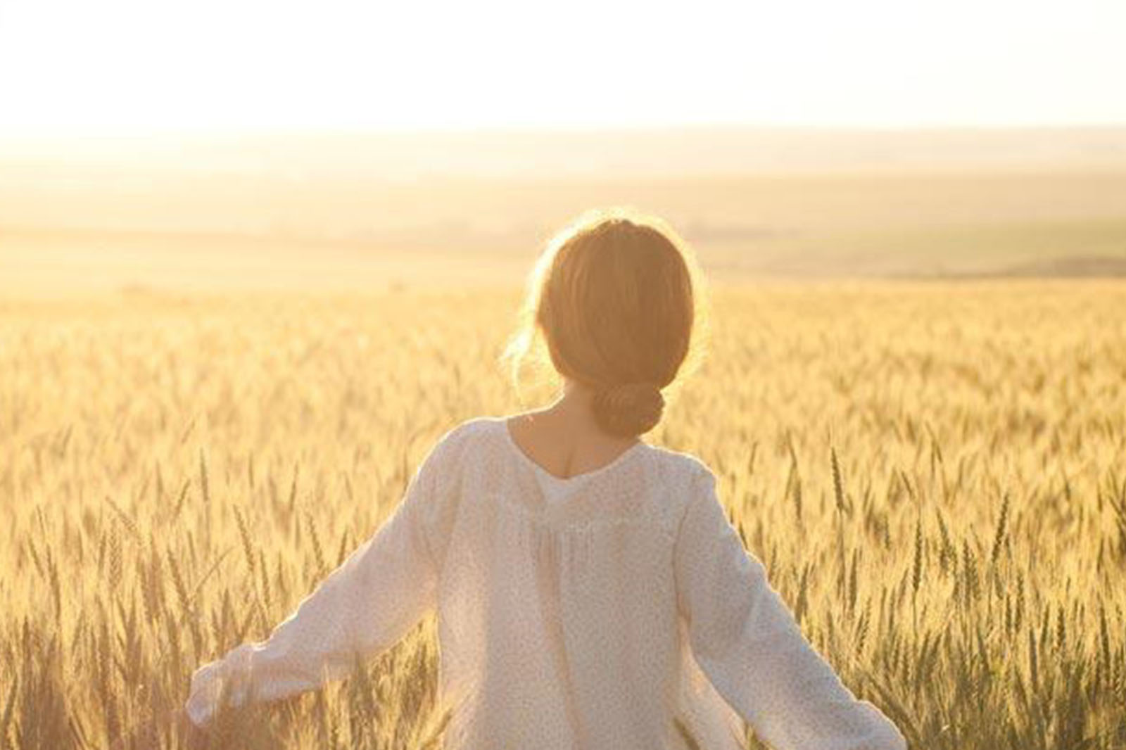 woman walking through a field of wheat in sunshine